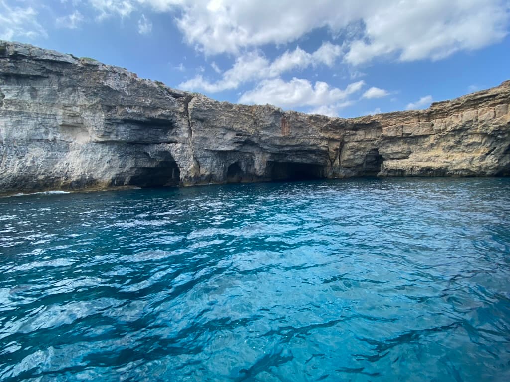 Kemmuna's (Comino's) honeycomb limestone coast from the water — multiple cave and cavern openings accessible on a single dive