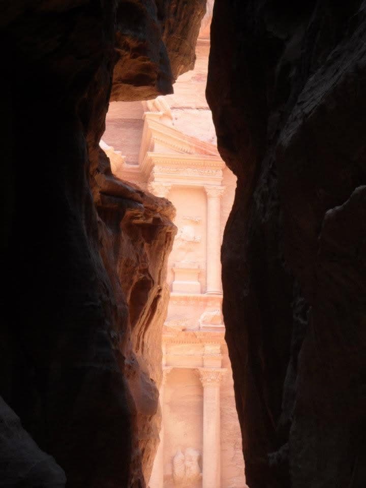 The Treasury glimpsed through the final narrows of the Siq — the carved façade visible as the canyon opens