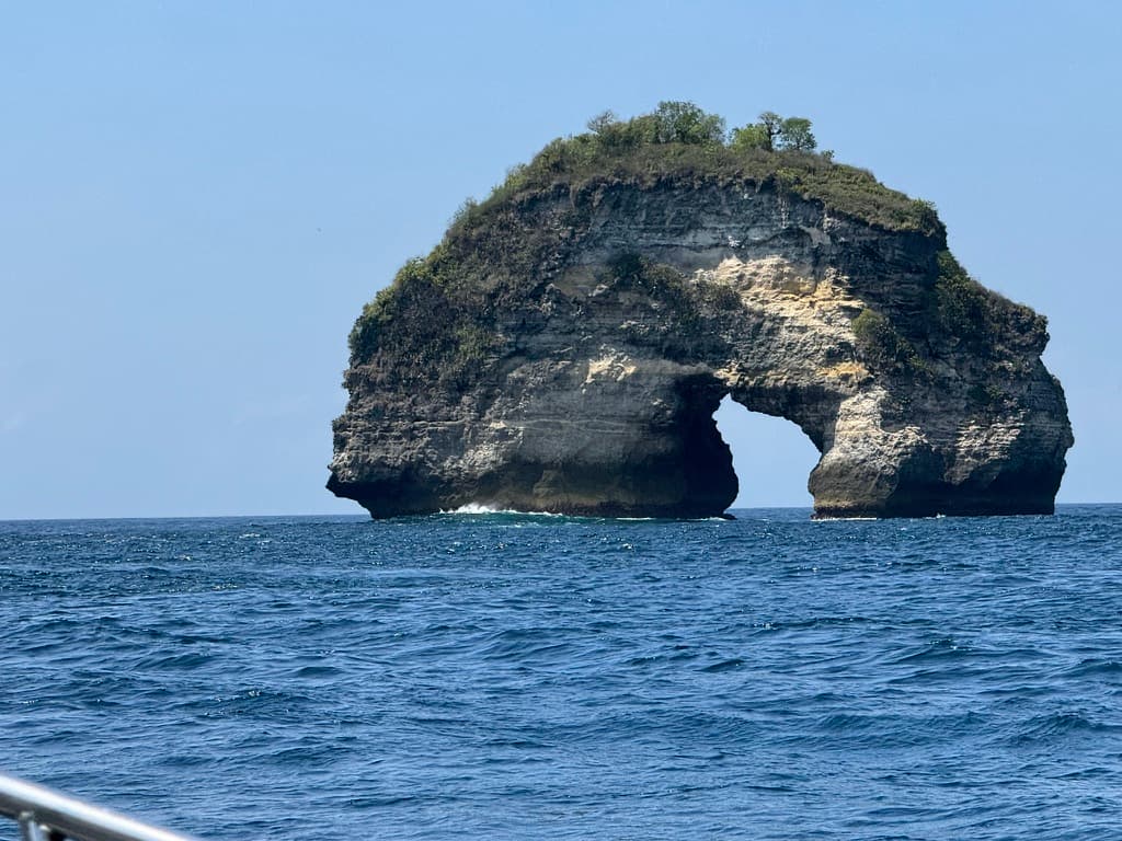 The natural arch rock formation rising from the Bali Strait — a navigation landmark and cleaning station below