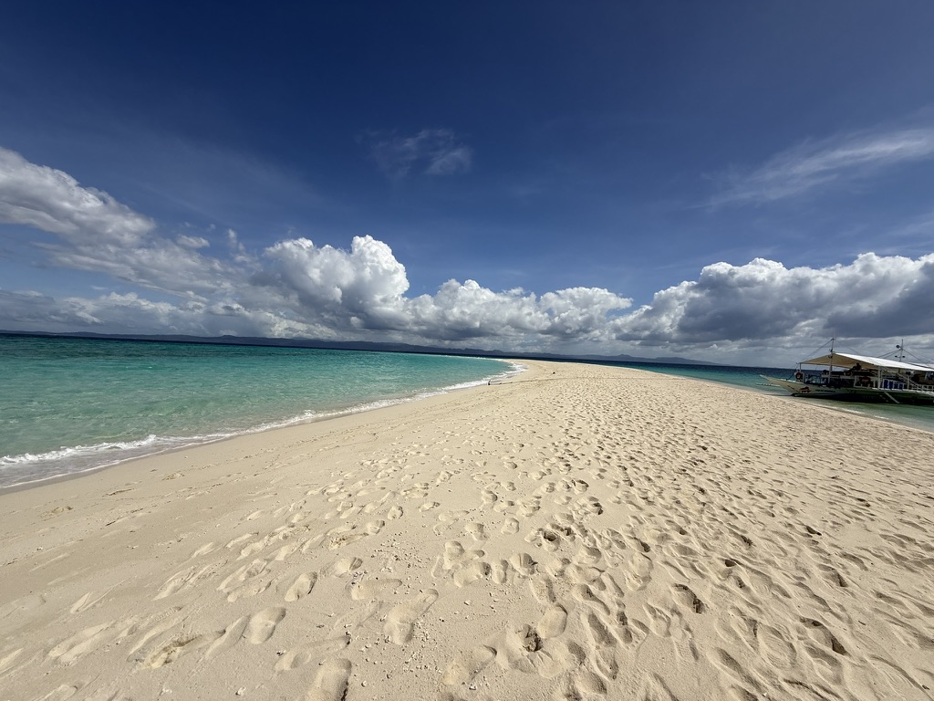 Kalanggaman Island's sandbar — the narrow white sand spit extending into open turquoise water, almost completely deserted at midday