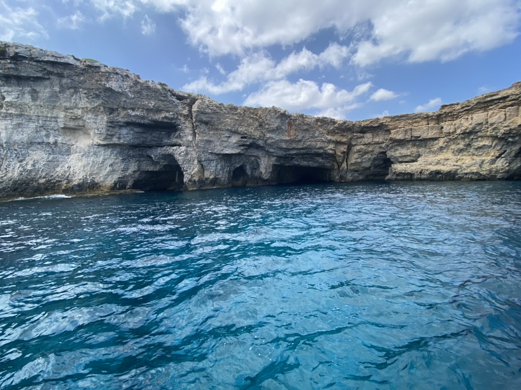 Comino's north coast from the water — multiple cave entrances cut into the limestone, each leading to a different dive